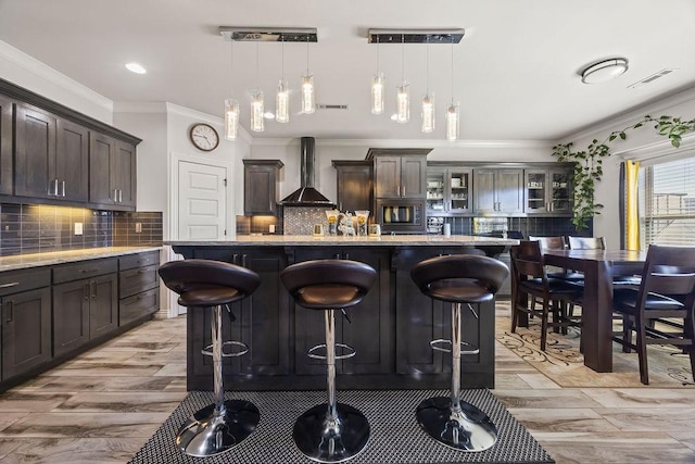 kitchen with visible vents, a kitchen bar, wall chimney exhaust hood, crown molding, and dark brown cabinets