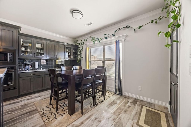 dining area with baseboards, visible vents, light wood finished floors, and ornamental molding