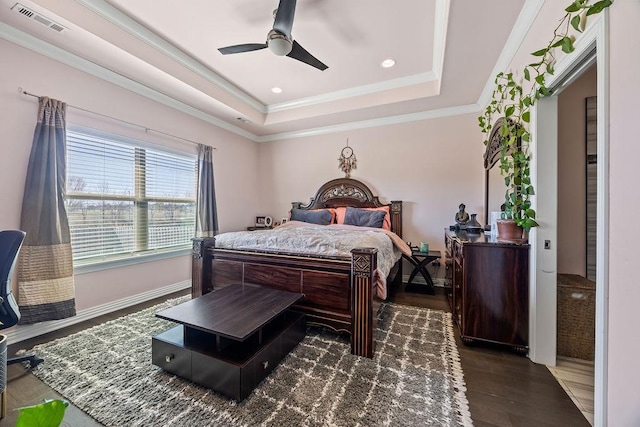 bedroom with wood finished floors, visible vents, baseboards, crown molding, and a raised ceiling