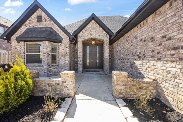 doorway to property featuring french doors, brick siding, and roof with shingles