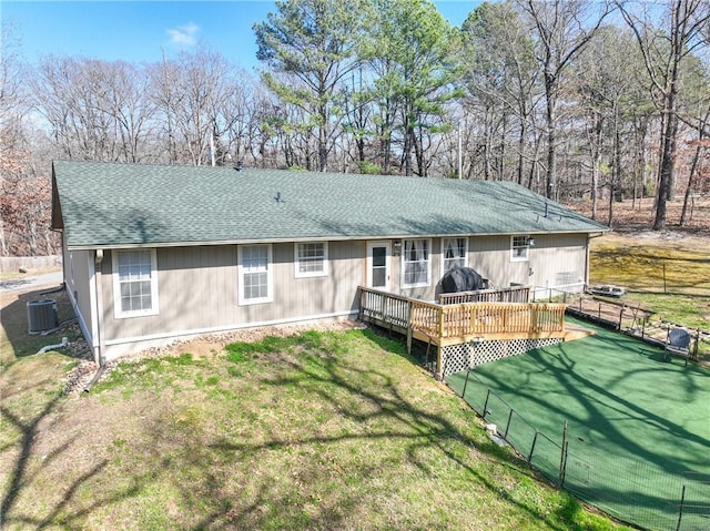 rear view of property featuring a shingled roof, fence, central AC unit, a lawn, and a deck