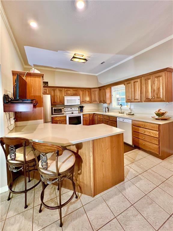 11 Saint Andrews Lane Holiday Island Unit 9, Holiday Island, AR 72631 - kitchen featuring white appliances, crown molding, a breakfast bar area, light countertops, and brown cabinets