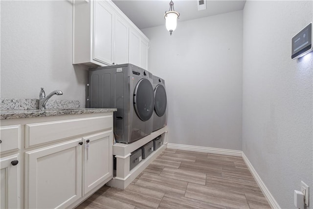 laundry area with visible vents, light wood finished floors, baseboards, cabinet space, and washer and dryer