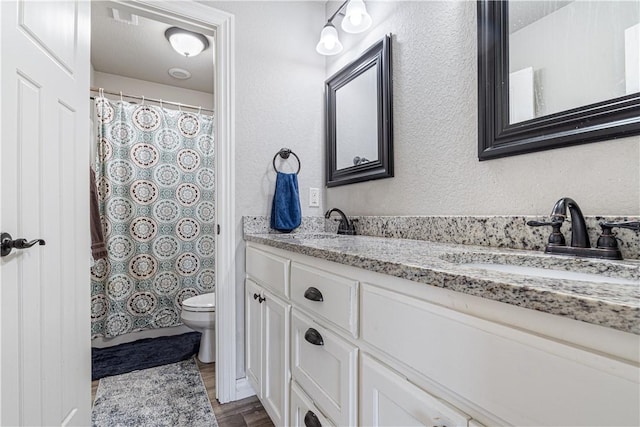 full bath with wood finished floors, double vanity, a sink, toilet, and a textured wall