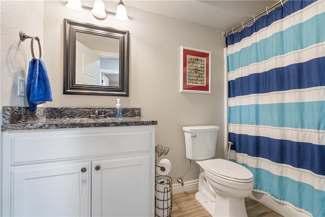 full bathroom with toilet, curtained shower, wood finished floors, vanity, and a textured wall