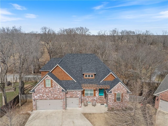 view of front facade featuring a shingled roof, concrete driveway, brick siding, and fence