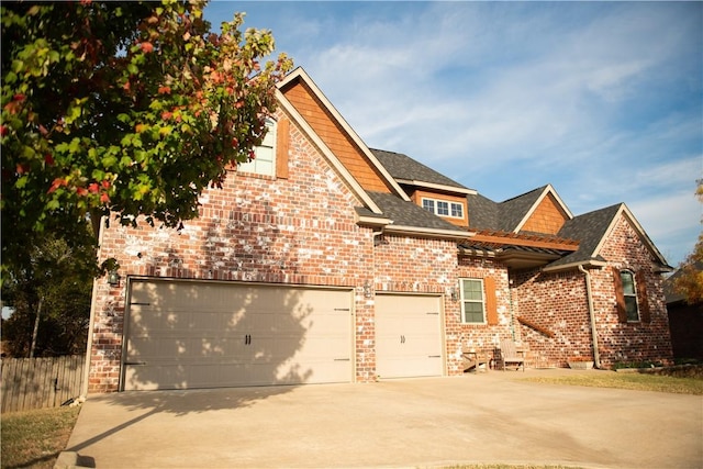 view of front of house with driveway, fence, roof with shingles, an attached garage, and brick siding