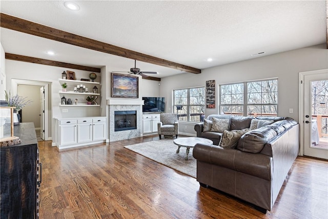 living room featuring a glass covered fireplace, beam ceiling, wood finished floors, and a textured ceiling