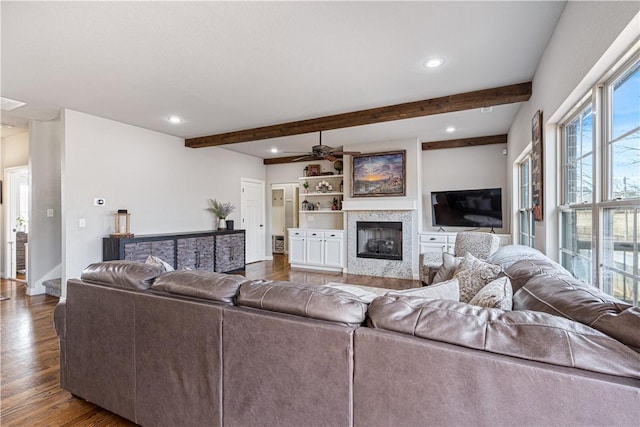 living area featuring beam ceiling, a glass covered fireplace, recessed lighting, and wood finished floors