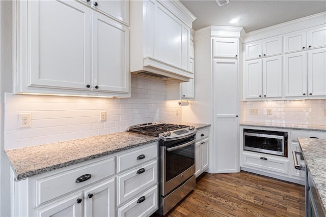 kitchen with light stone counters, dark wood-style floors, stainless steel appliances, white cabinetry, and tasteful backsplash