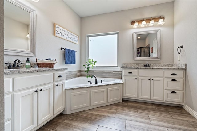 full bathroom featuring wood tiled floor, two vanities, a garden tub, and a sink