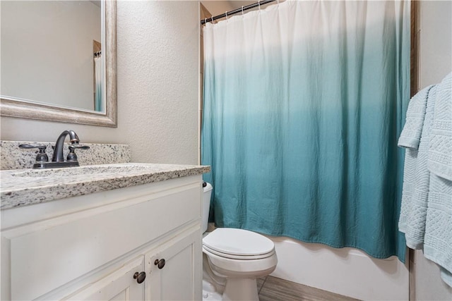 bathroom featuring shower / bath combo with shower curtain, toilet, a textured wall, wood finished floors, and vanity