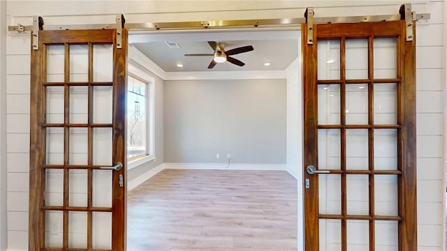 empty room featuring ceiling fan, wood finished floors, a barn door, and ornamental molding