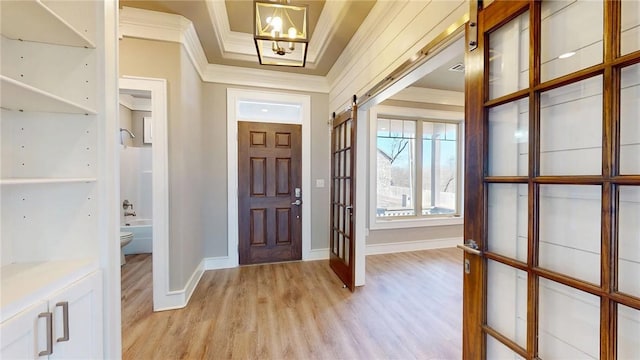 entrance foyer with baseboards, light wood-style flooring, crown molding, a raised ceiling, and a chandelier