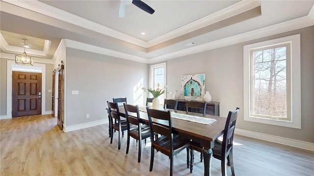 dining space with light wood-type flooring, a tray ceiling, baseboards, and ornamental molding