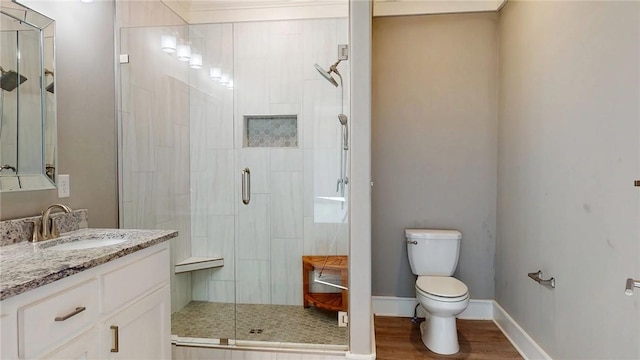 bathroom featuring toilet, a stall shower, wood finished floors, baseboards, and vanity