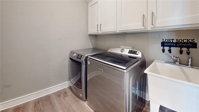 laundry room with washing machine and clothes dryer, baseboards, light wood-style floors, cabinet space, and a sink