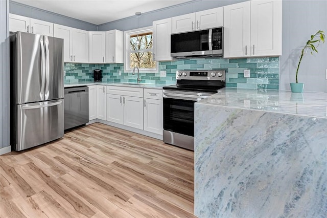 kitchen featuring light wood finished floors, tasteful backsplash, white cabinets, stainless steel appliances, and a sink