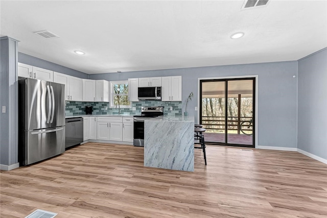 kitchen featuring backsplash, stainless steel appliances, light wood-style floors, white cabinets, and light countertops