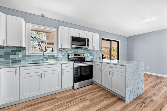 kitchen featuring light wood-style flooring, a peninsula, stainless steel appliances, and a sink