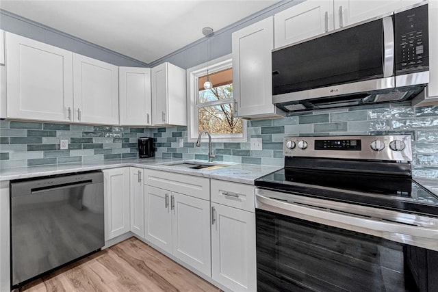 kitchen with tasteful backsplash, light wood-type flooring, appliances with stainless steel finishes, white cabinets, and a sink