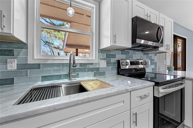 kitchen featuring a sink, backsplash, white cabinetry, appliances with stainless steel finishes, and light stone countertops