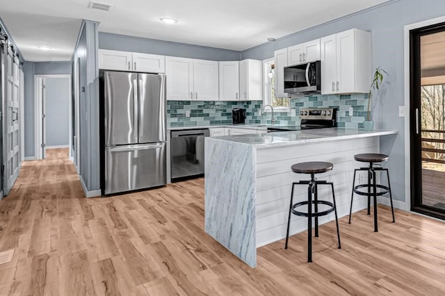 kitchen featuring a peninsula, white cabinets, light wood-style flooring, and appliances with stainless steel finishes