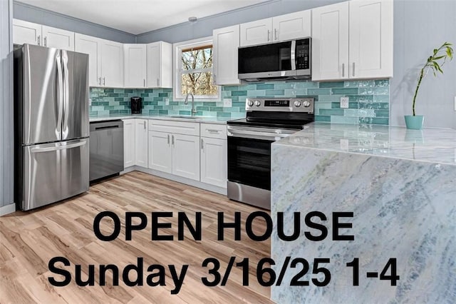 kitchen featuring light wood-style flooring, a sink, appliances with stainless steel finishes, white cabinetry, and tasteful backsplash