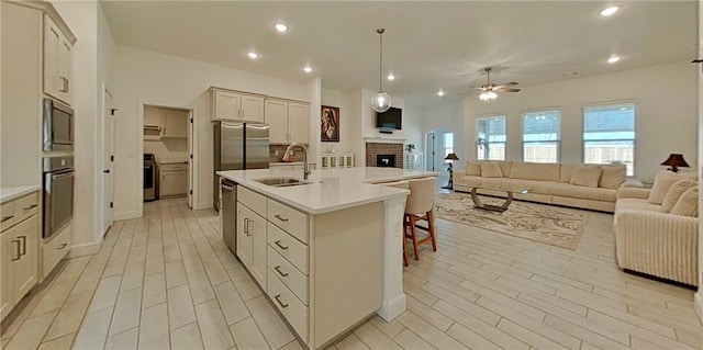 kitchen with a center island with sink, a sink, open floor plan, stainless steel appliances, and light countertops