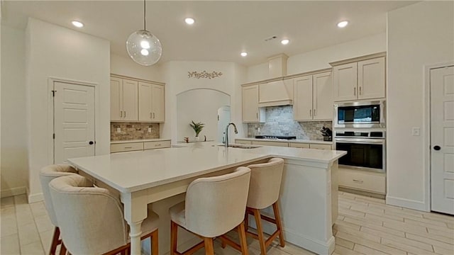 kitchen featuring a sink, light countertops, arched walkways, stainless steel appliances, and a kitchen island with sink