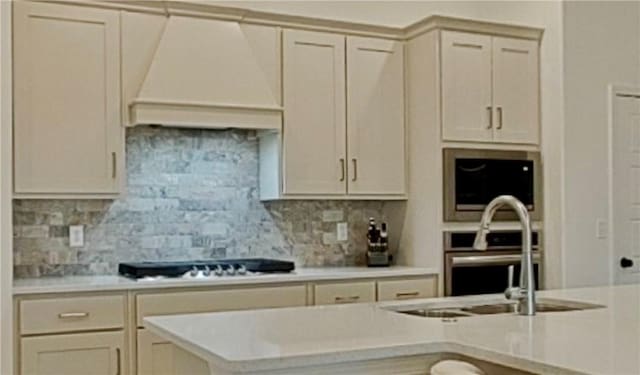 kitchen featuring tasteful backsplash, light countertops, custom exhaust hood, gas stovetop, and a sink