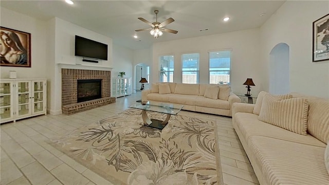 living room with a ceiling fan, wood finished floors, recessed lighting, arched walkways, and a brick fireplace