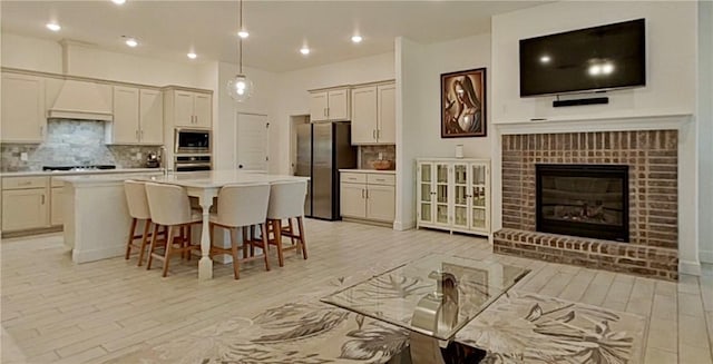 kitchen featuring a kitchen bar, light countertops, decorative backsplash, a fireplace, and stainless steel appliances