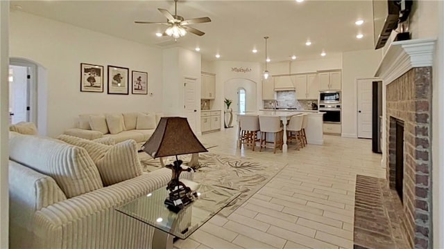 living room featuring a brick fireplace, recessed lighting, a ceiling fan, and arched walkways