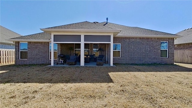 rear view of property with brick siding, roof with shingles, a patio, and fence