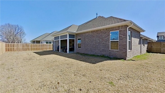 rear view of property with brick siding, a fenced backyard, and a shingled roof