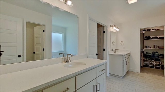 full bathroom with a spacious closet, two vanities, and a sink