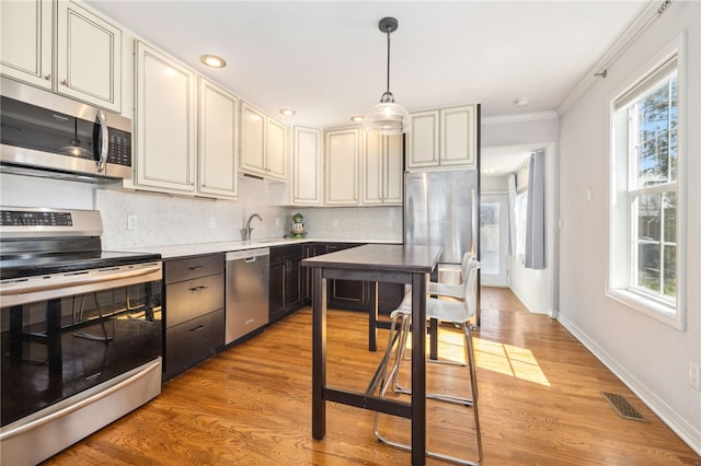 kitchen with tasteful backsplash, light wood finished floors, appliances with stainless steel finishes, and ornamental molding