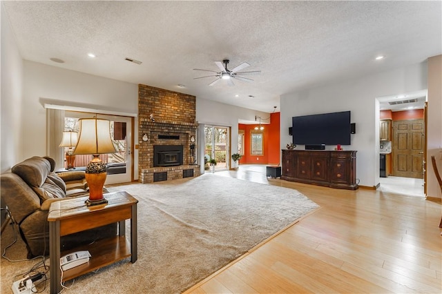 living area featuring a ceiling fan, light wood-style floors, visible vents, and a textured ceiling