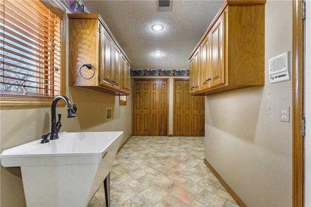 washroom featuring a textured ceiling, hookup for a washing machine, baseboards, cabinet space, and stone finish flooring