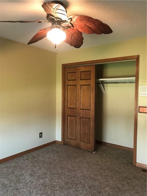 unfurnished bedroom with a closet, dark carpet, a textured ceiling, and baseboards