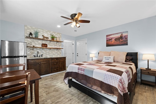 bedroom featuring light wood finished floors, a ceiling fan, freestanding refrigerator, and a sink