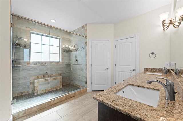 bathroom featuring an inviting chandelier, double vanity, a stall shower, and a sink