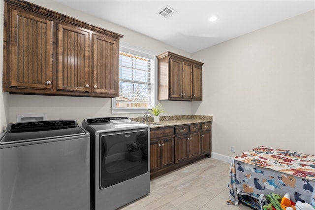 washroom featuring visible vents, baseboards, cabinet space, a sink, and independent washer and dryer