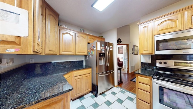 kitchen with dark stone countertops, light floors, appliances with stainless steel finishes, and light brown cabinetry