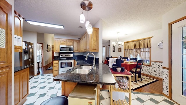 kitchen with a notable chandelier, a sink, a textured ceiling, appliances with stainless steel finishes, and light floors