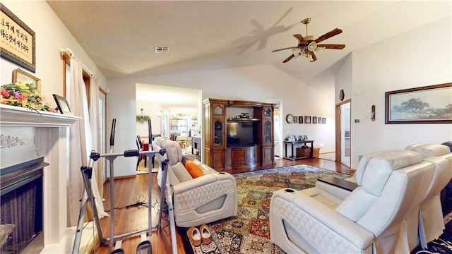 living area with visible vents, ceiling fan with notable chandelier, wood finished floors, a fireplace, and vaulted ceiling