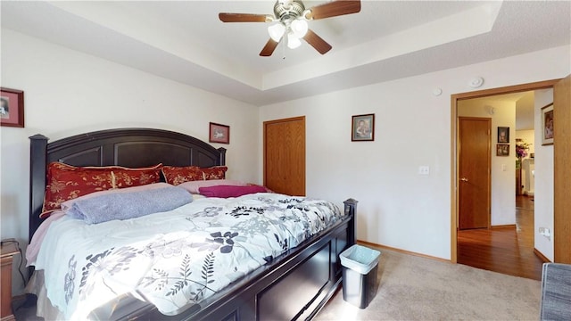 bedroom featuring carpet flooring, baseboards, a tray ceiling, and a ceiling fan