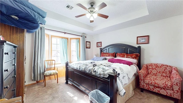 bedroom featuring a tray ceiling, visible vents, light colored carpet, and a textured ceiling