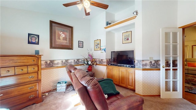 living area with a wainscoted wall, light carpet, ceiling fan, and wallpapered walls